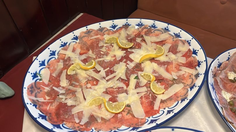 Dünn geschnittenes Fleisch mit Zitronenscheiben und Parmesan auf einem Teller.