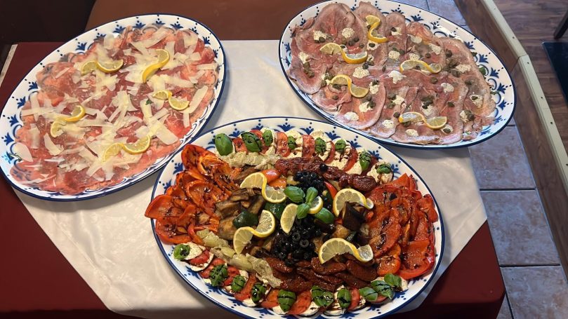 Drei Teller mit verschiedenen Fleisch- und Fischplatten, garniert mit Zitrone und Gemüse.